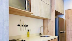 A kitchen with a microwave on a wooden shelf, a sink with a faucet, and a bottle of oil. - Majestic Loft in Santa Barbara (Bogotá)