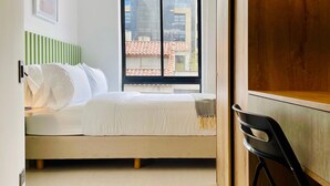 A bedroom with a bed, a window with a view of buildings, a chair, and a wooden cabinet. - Majestic Loft in Santa Barbara (Bogotá)
