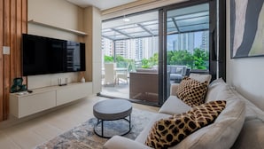 A modern living room with a flat-screen TV, sofa with giraffe-patterned pillows, and a glass door leading to a balcony with outdoor furniture. - w Radiant 1BR w Modern Balcony in San Francisco (Panama City)