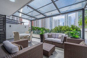 A modern outdoor patio with wicker furniture, a glass ceiling, and a view of high-rise buildings. - w Radiant 1BR w Modern Balcony in San Francisco (Panama City)