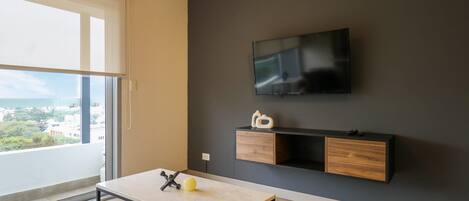 Una sala de estar moderna con un ventanal grande, un televisor de pantalla plana montado en la pared, una mesa de centro de madera y un mueble de entretenimiento minimalista.