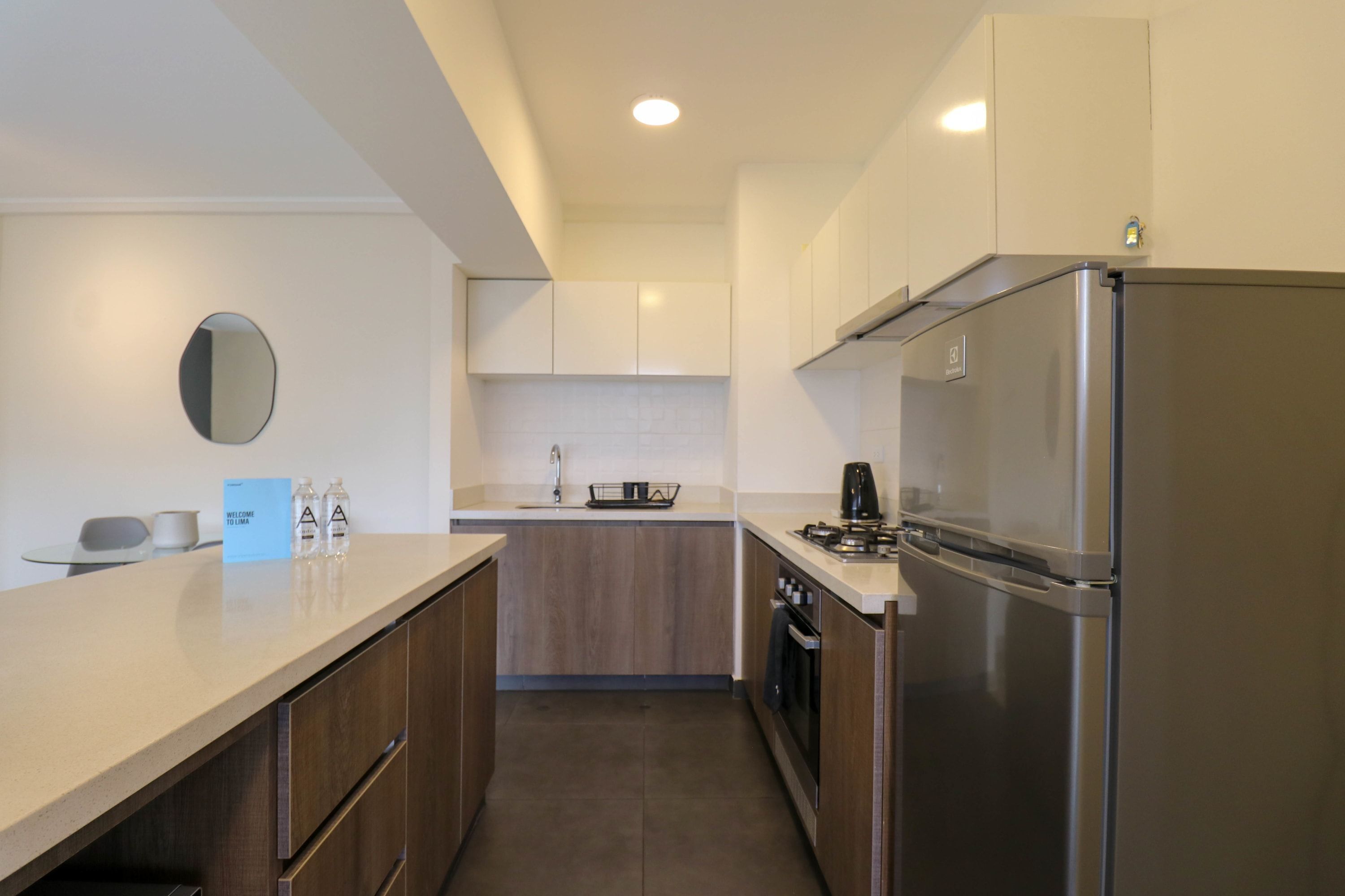 A modern kitchen with a stainless steel refrigerator, wooden cabinets, and a white countertop.