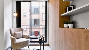 A modern room with a large window, a beige armchair, a small table, and a wooden cabinet with shelves. - Lovely Loft With Modern Deco in Chapinero (Bogotá)