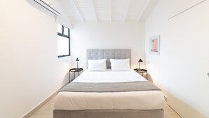 Ett hotellrum med en stor säng, en grå sänggavel, två sängbord med lampor och ett fönster på en av väggarna.