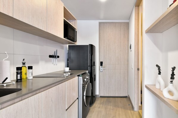 A modern kitchen with wooden cabinets, a built-in microwave, a refrigerator, and a washing machine.