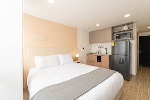 A hotel room with a large bed, a kitchenette with a refrigerator and microwave, and a small wooden cabinet.
