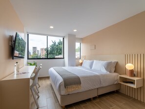 A modern bedroom with a large bed, bedside tables, a desk, and a TV mounted on the wall. - w Beautiful Loft in Laureles (Medellín)