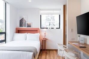 A hotel room with a bed, a desk with a chair, a lamp, a TV, and a window with a view of buildings. - w Splendid Loft w Fantastic Deco in Bogota (Bogotá)