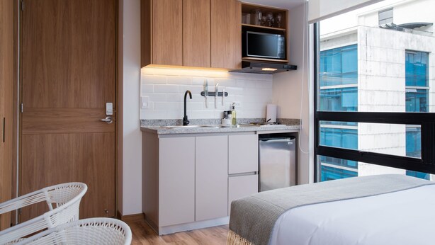 A compact kitchen with wooden cabinets, a microwave, and a dishwasher. There is a window providing a view of the cityscape. - w Splendid Loft w Fantastic Deco in Bogota (Bogotá)