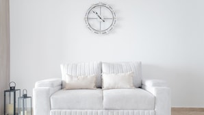 Een witte bank met twee kussens, een wandklok en twee zwarte lantaarns.