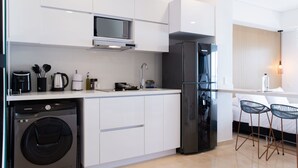 Een moderne keuken met witte kasten, een ingebouwde magnetron, een roestvrijstalen koelkast, een wasmachine en een bar met twee stoelen.
