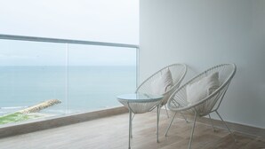 Een balkon met een glazen tafel en twee witte rieten stoelen, met uitzicht op een strand en de oceaan.