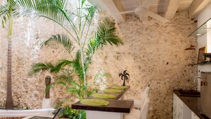 Una cocina con pared de piedra, una silla blanca y una encimera de madera con individuales verdes.