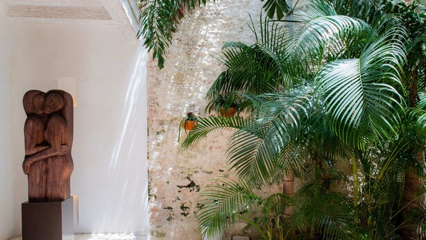 Una habitación con pared de piedra, una escultura de madera y exuberantes plantas verdes.
