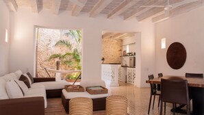 Una sala moderna con un sofá, otomanas, una mesa de comedor y sillas. Se ve una pared de piedra y vegetación al exterior.