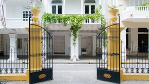 Un edificio blanco con un acceso cubierto, un camino de entrada con portones y un balcón con plantas.
