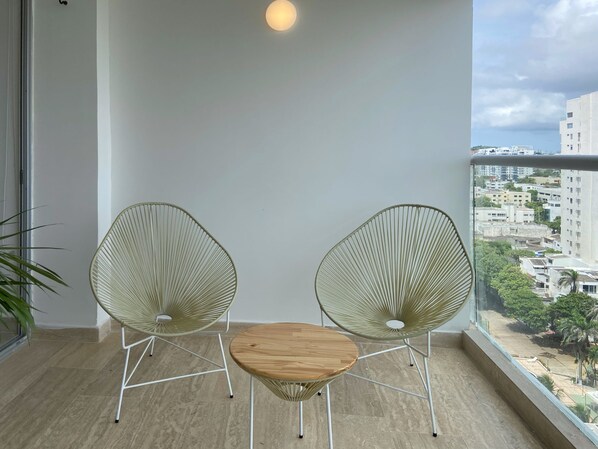 Un balcon avec deux chaises en fil de fer vert et une petite table en bois.