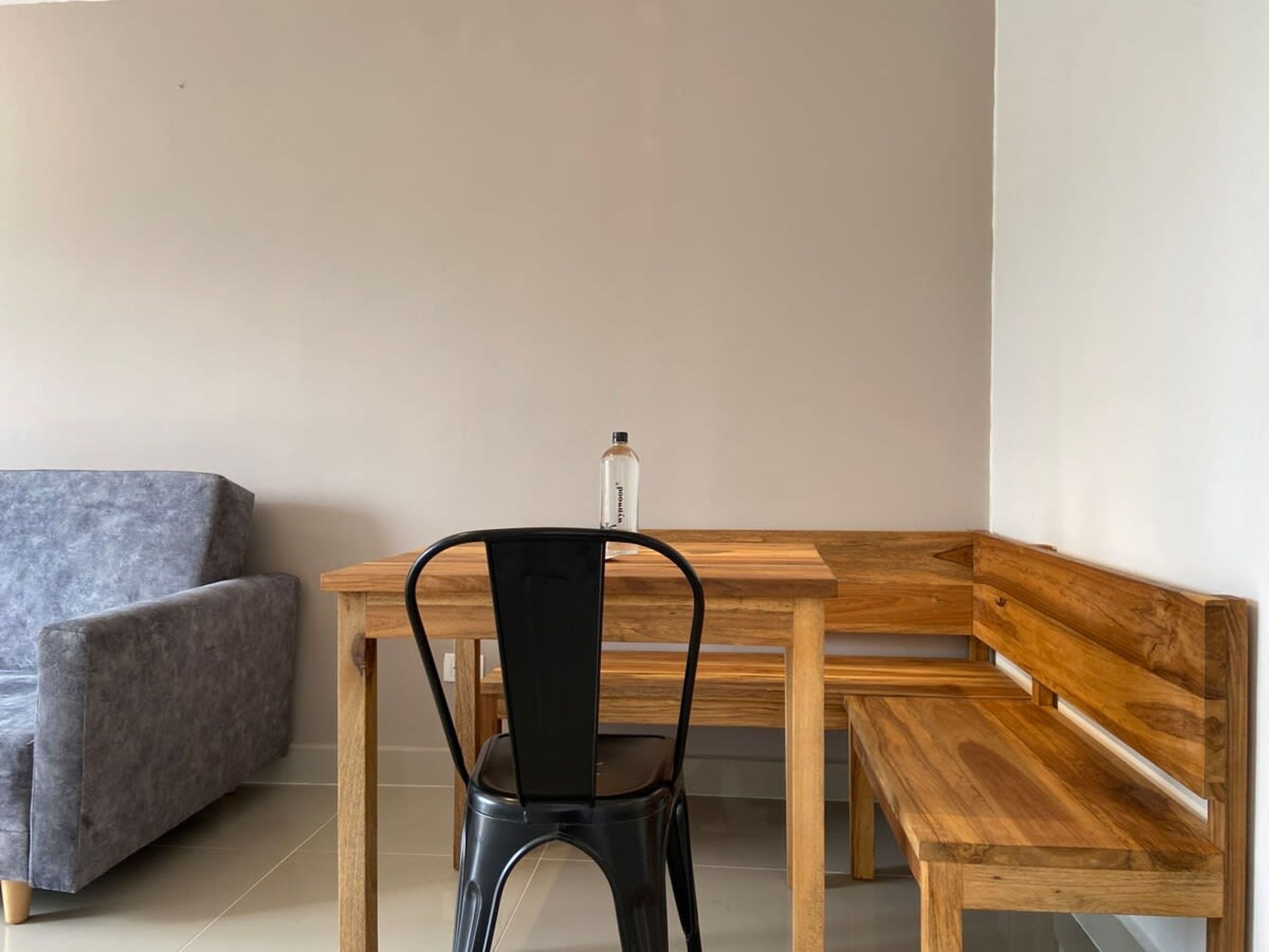 Un'area salotto angolare con un tavolo in legno e una panca, una sedia in metallo nero e un divano grigio.