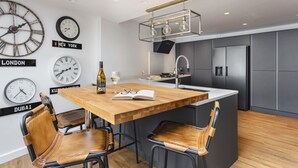 A modern kitchen with a central island, bar stools, and wall clocks displaying different cities.