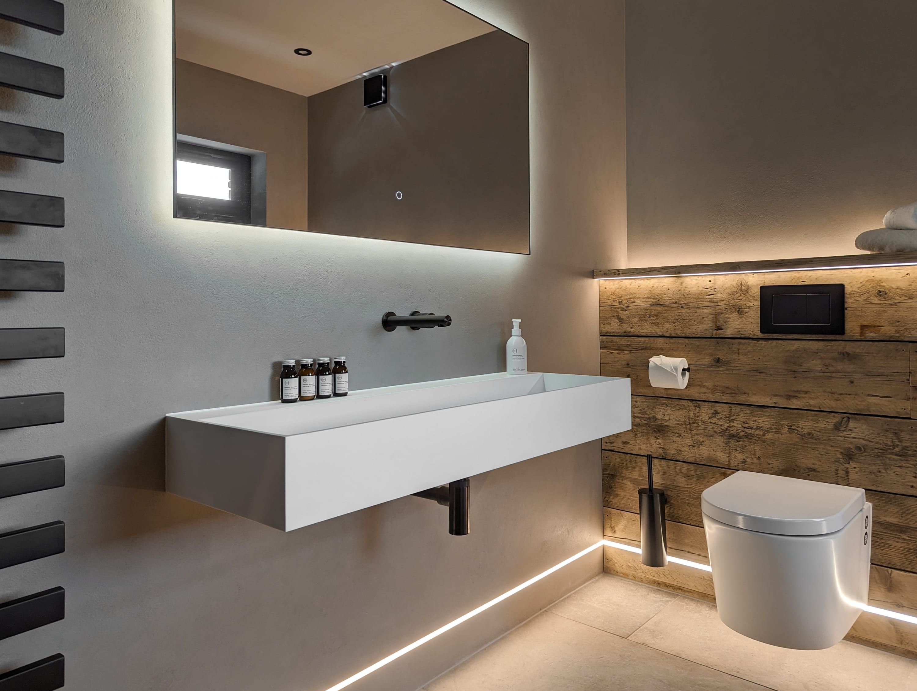 Un baño moderno con un lavamanos blanco, espejo y paneles de madera en la pared.