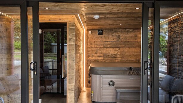 Een moderne spa-ruimte met een bubbelbad, glazen deuren en een stenen muur.