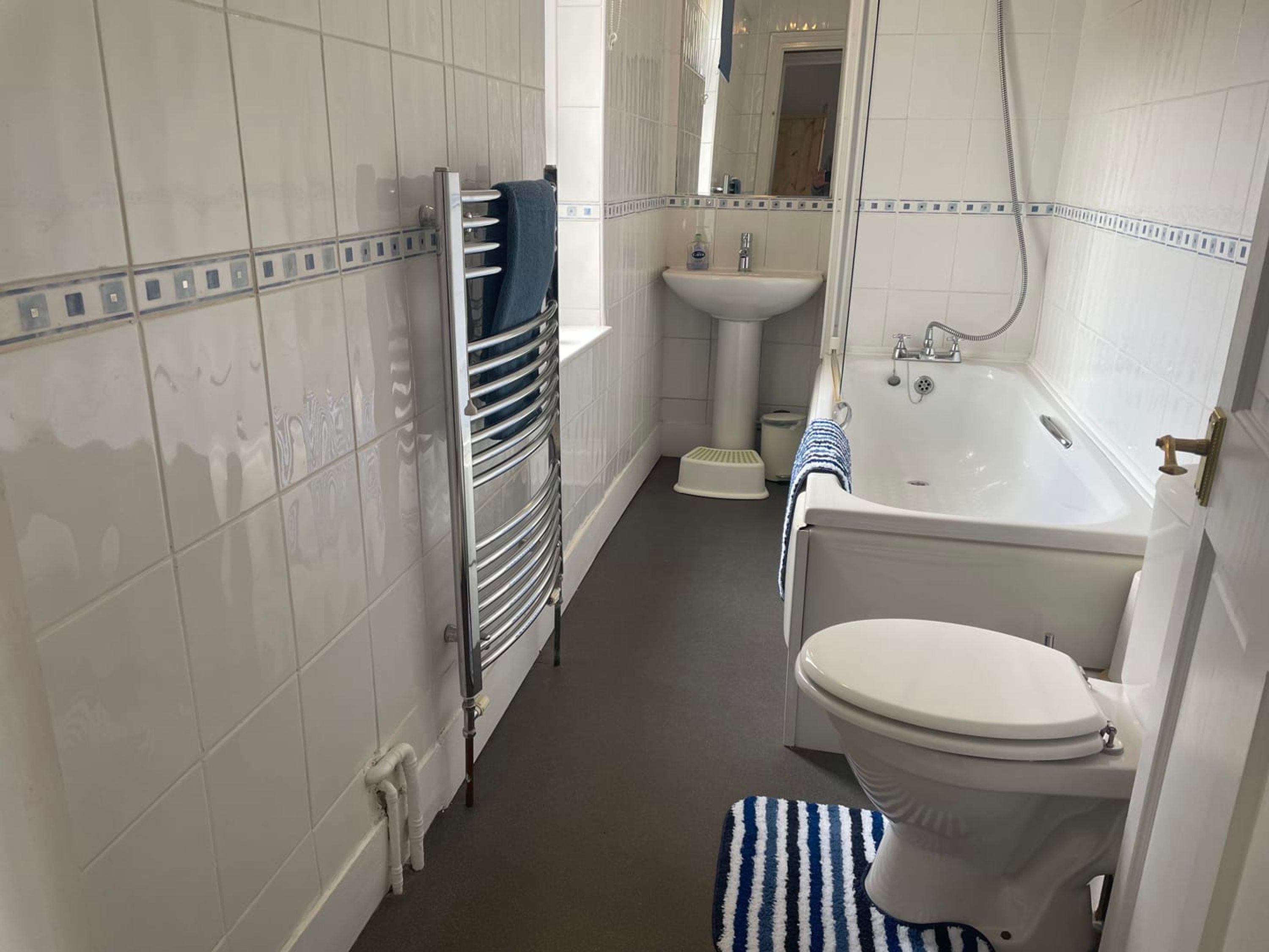 A bathroom with white tiled walls, a white sink, a bathtub, and a toilet.