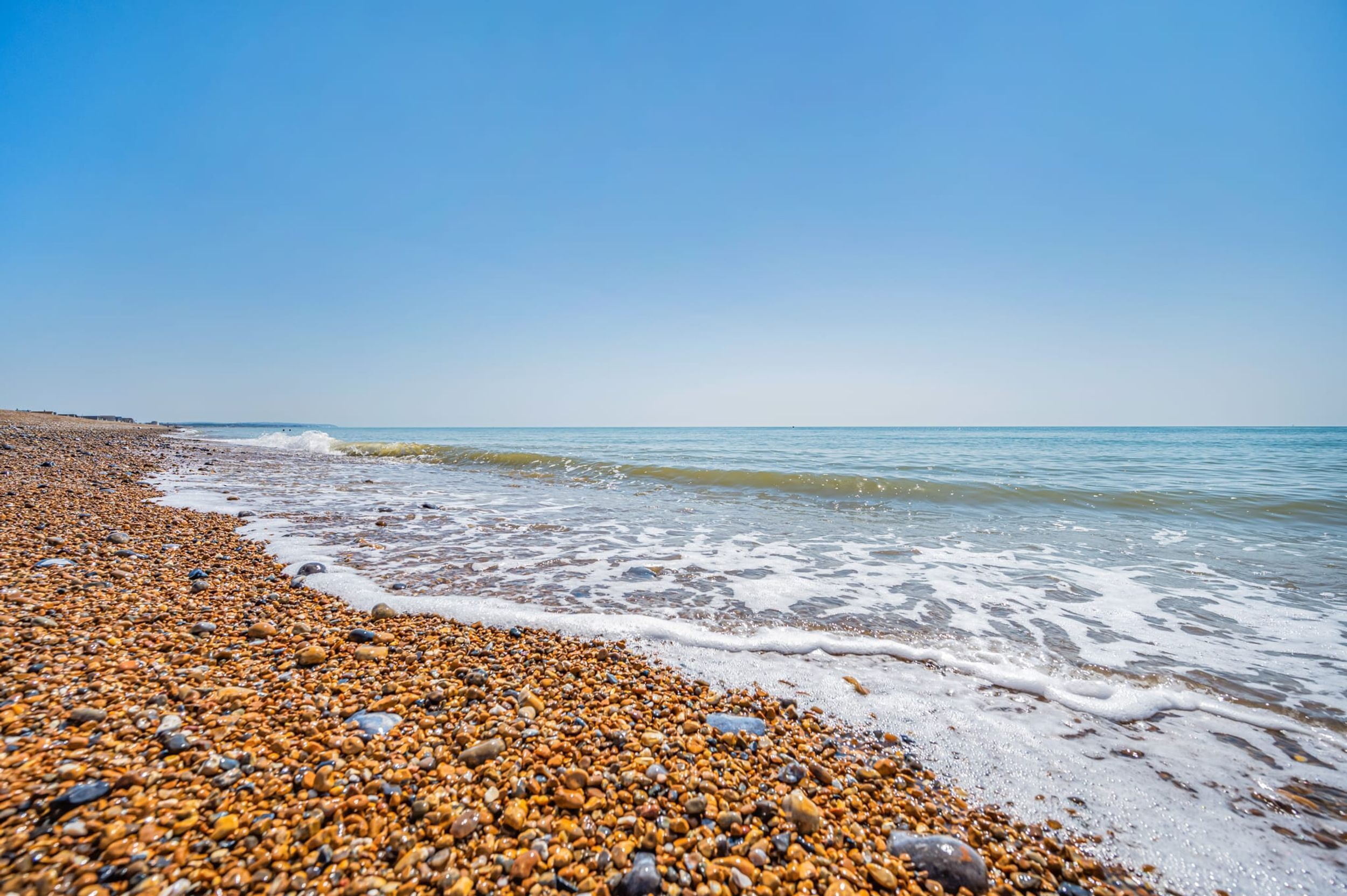A pebbled beach with clear blue water and a distant shoreline.