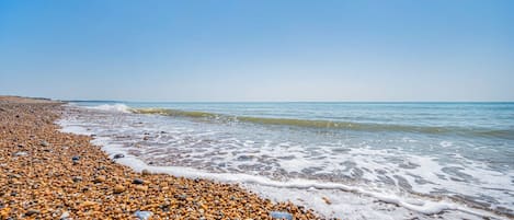 A pebbled beach with clear blue water and a distant shoreline.