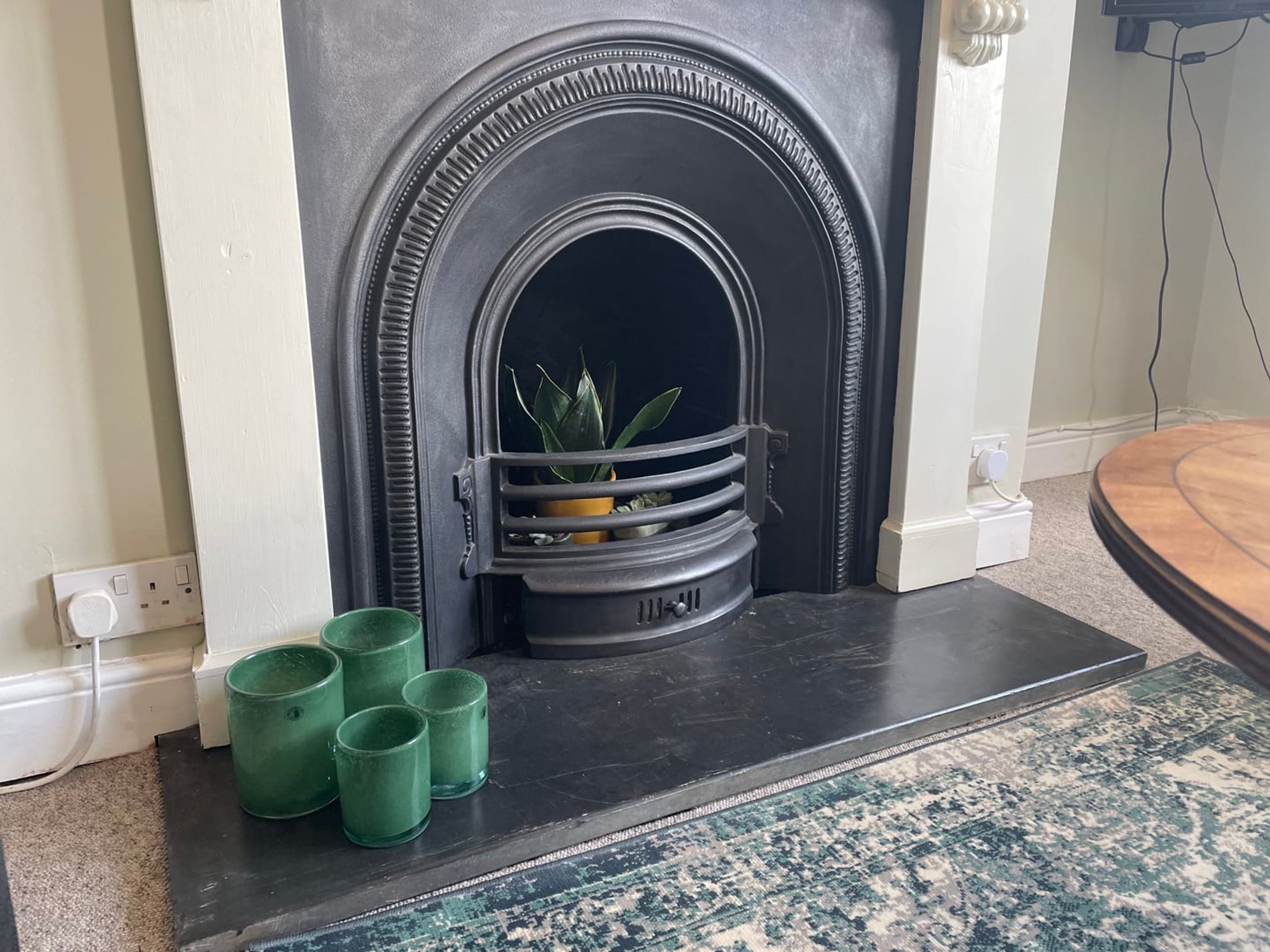 A fireplace with a black surround, a potted plant, and green candle holders on the mantel.