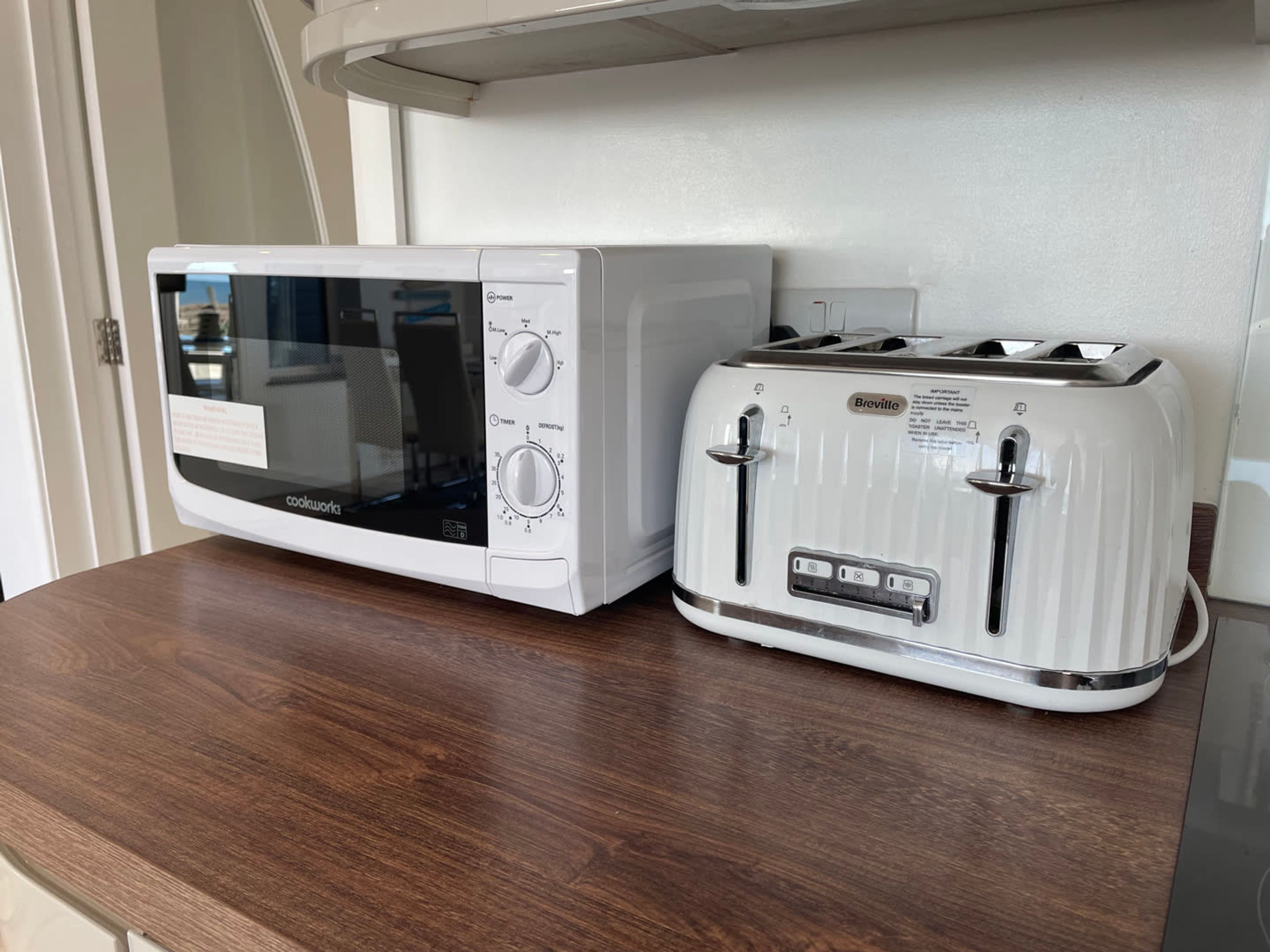 A Breville toaster and a cookware microwave on a wooden countertop.