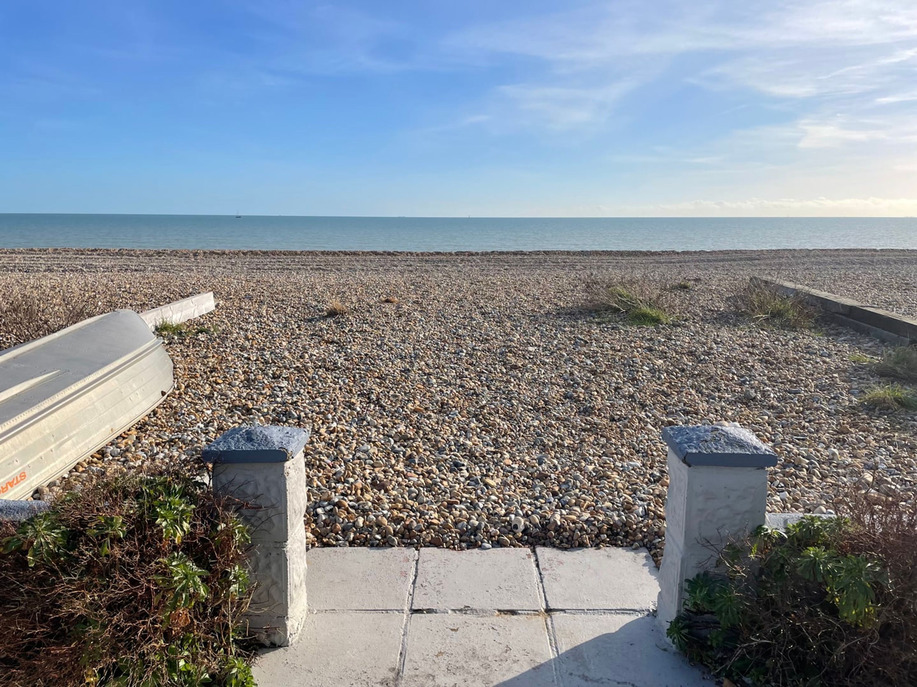 A pebbled beach with a concrete pathway leading to the sea.