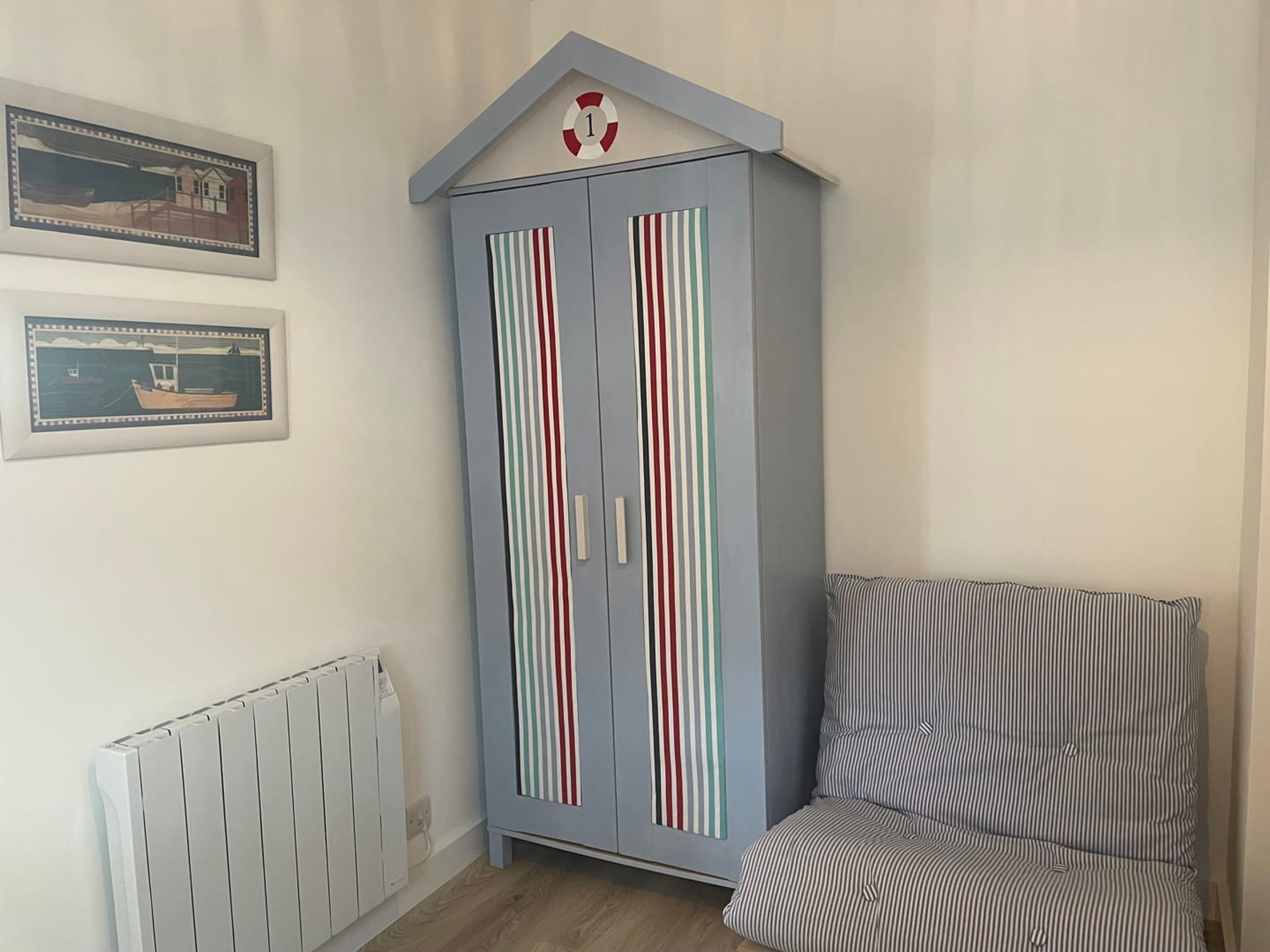 A room with a striped armchair, a blue cabinet with vertical stripes, and two framed pictures on the wall.