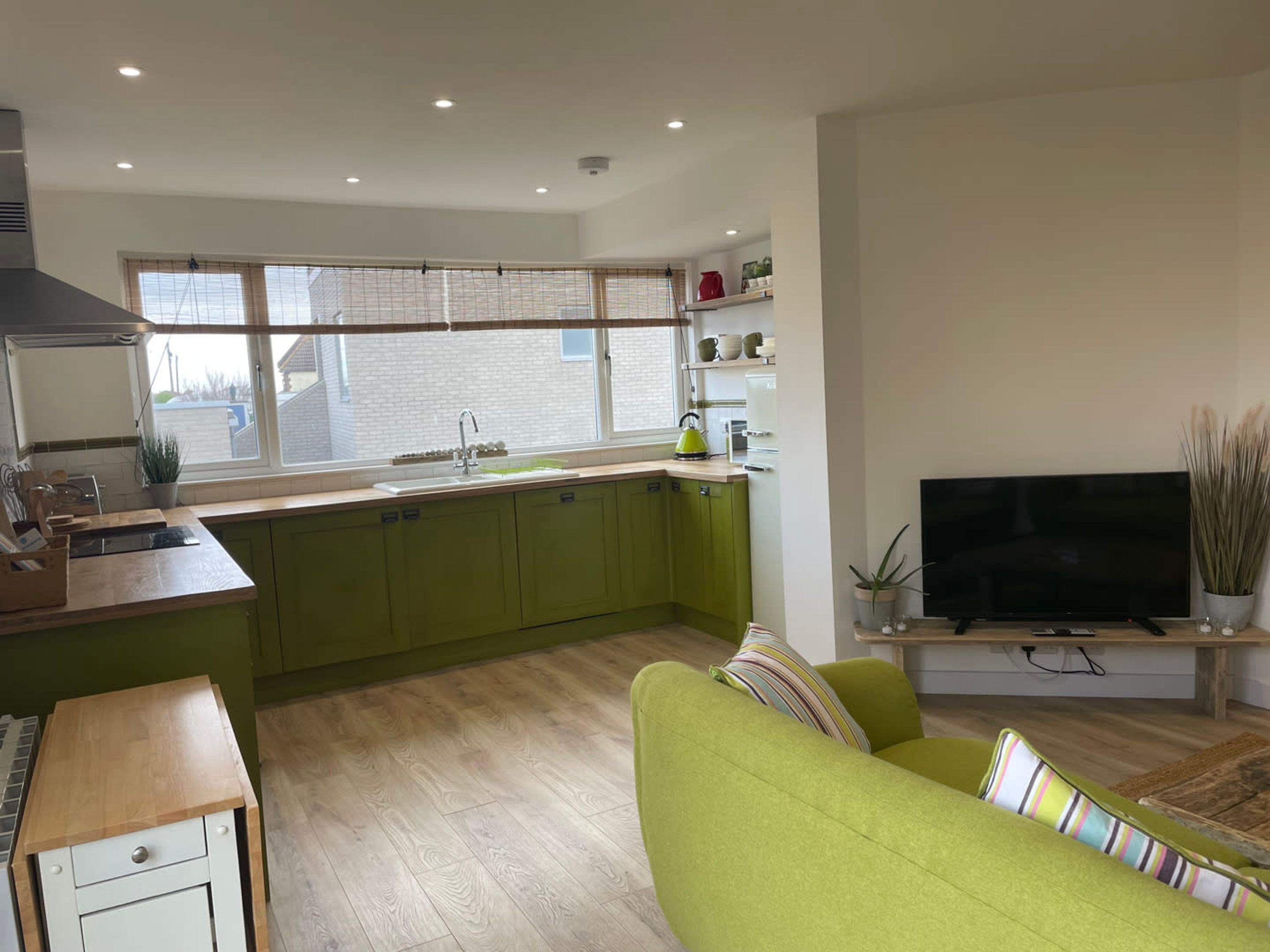 Une cuisine moderne avec des meubles de couleur verte, une grande fenêtre et un téléviseur à écran plat posé sur un meuble en bois.