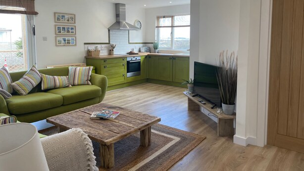 A modern living room with a green sofa, a wooden coffee table, and a television on a stand. - The Crabshack Cottage Normans Bay Pevensey (Pevensey)