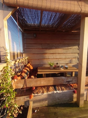 A wooden deck with a bench, a table with a plant, and a hanging plant. - The Crabshack Cottage Normans Bay Pevensey (Pevensey)