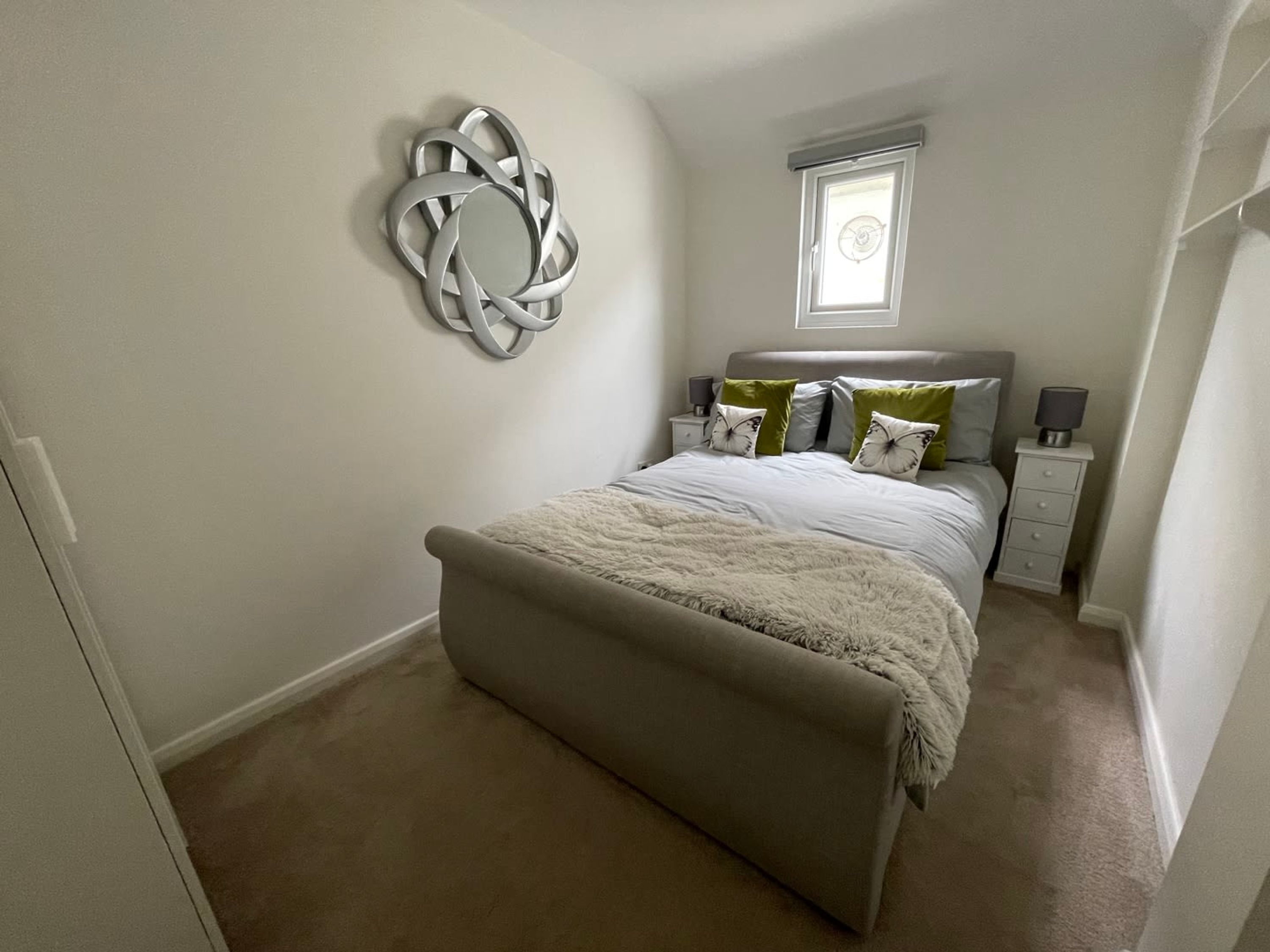 Une chambre à coucher comprenant un lit, une table de chevet, une commode, un élément de décoration murale et une fenêtre.