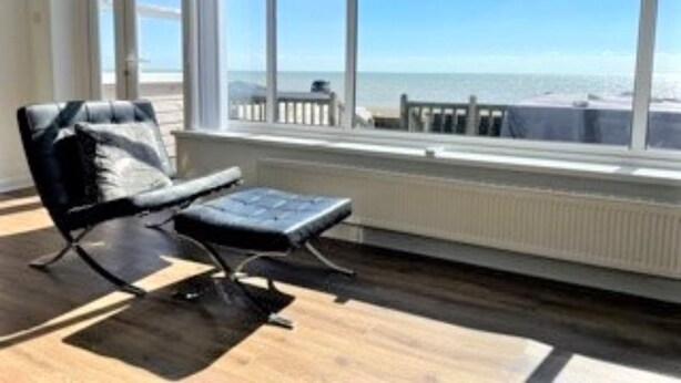 A room with a large window overlooking the sea, a black chair with a cushion, and a radiator under the window. - Exquisite Beachfront Residence With Luxurious Interiors The Cozy Clam Pevensey Bay (Pevensey)