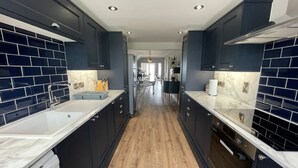 A modern kitchen with dark cabinetry, marble countertops, and a wooden floor. - Exquisite Beachfront Residence With Luxurious Interiors The Cozy Clam Pevensey Bay (Pevensey)