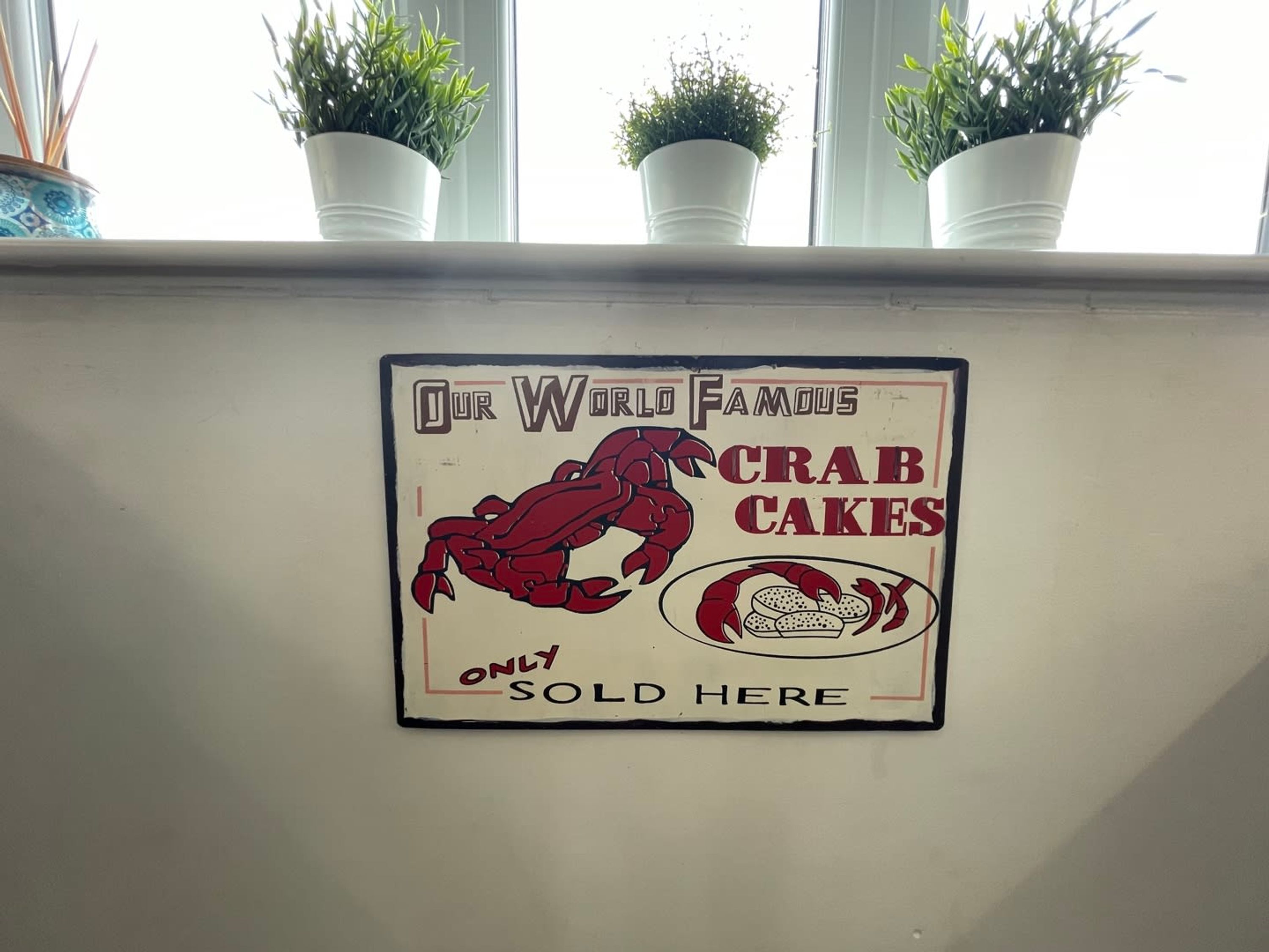 A wall sign advertising 'Our World Famous Crab Cakes' with a crab illustration and text stating 'Only Sold Here'.