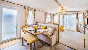 A cozy, well-lit room with a dining table set for two, a sofa with cushions, and a large window with curtains. - Your Ultimate Holiday Rental at Pevensey Bay (Pevensey)