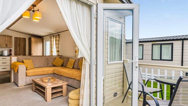 An open sliding door leading to a cozy living area with a sofa, coffee table, and a view of the adjacent building. - Your Ultimate Holiday Rental at Pevensey Bay (Pevensey)