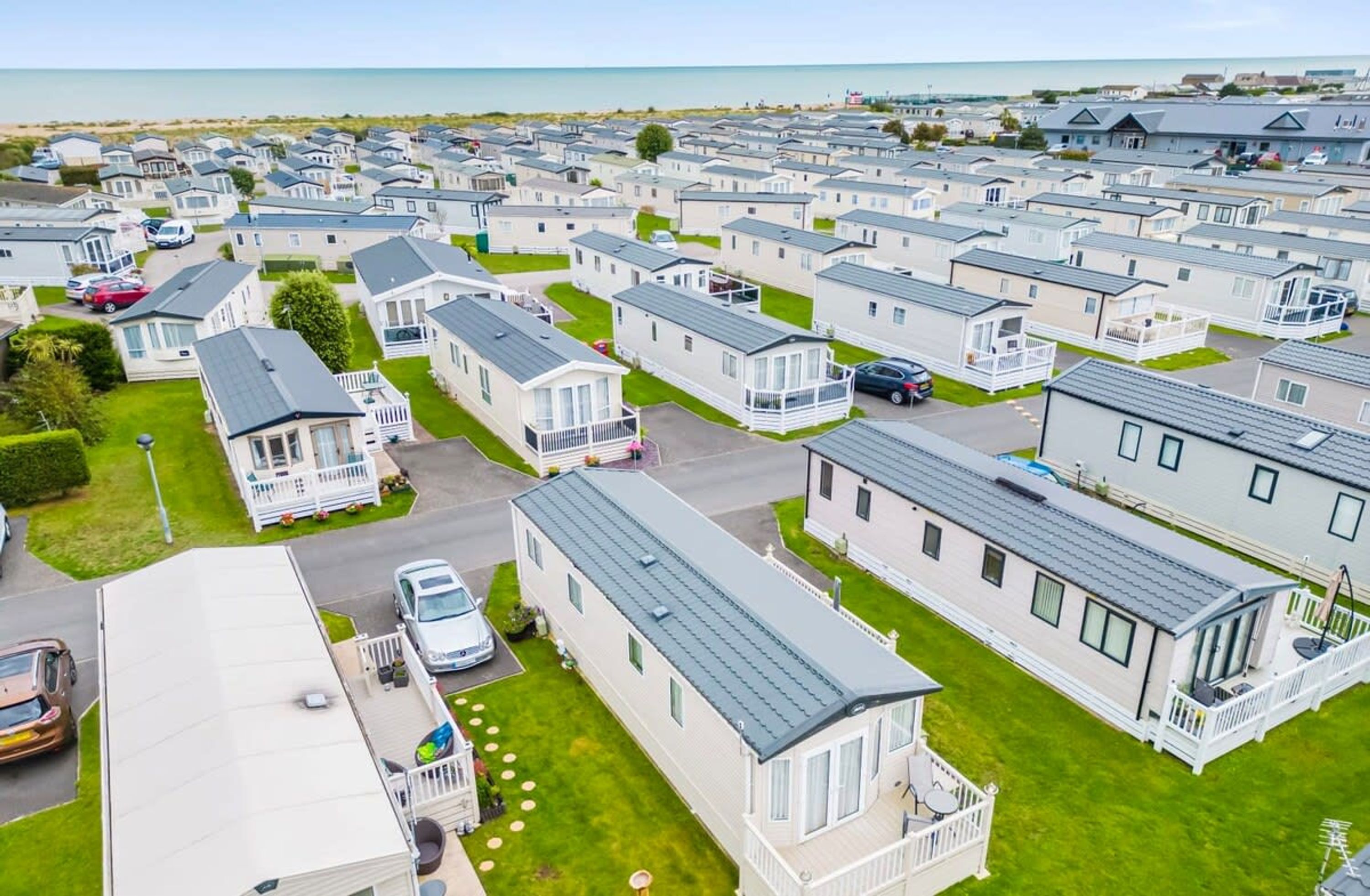 A large caravan park with multiple caravans and mobile homes, arranged in rows with grassy areas and a view of the sea in the background.