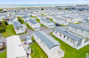 A large caravan park with multiple caravans and mobile homes, arranged in rows with grassy areas and a view of the sea in the background. - Your Ultimate Holiday Rental at Pevensey Bay (Pevensey)