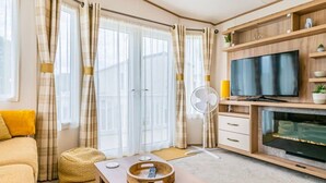 A modern living room with a sofa, a wooden coffee table, a flat-screen TV, and a fireplace. - Your Ultimate Holiday Rental at Pevensey Bay (Pevensey)