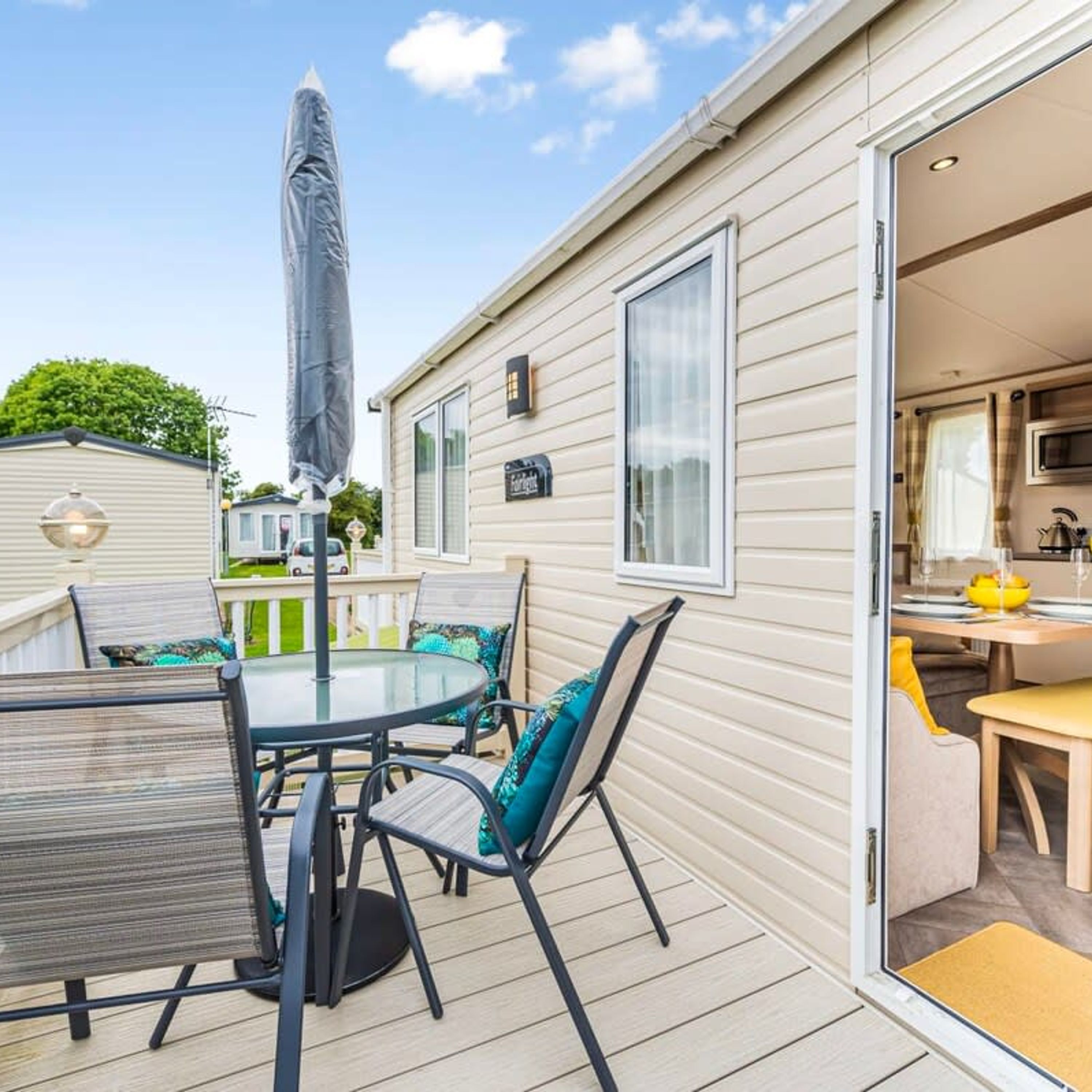 Casa móvil con patio que incluye mesa y sillas, una sombrilla y una puerta corrediza que da a una cocina.