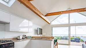 A modern kitchen with wooden beams, a large window, and a view of the sea.
