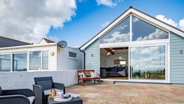 A modern house with a patio area featuring wicker furniture and a stone-tiled floor.