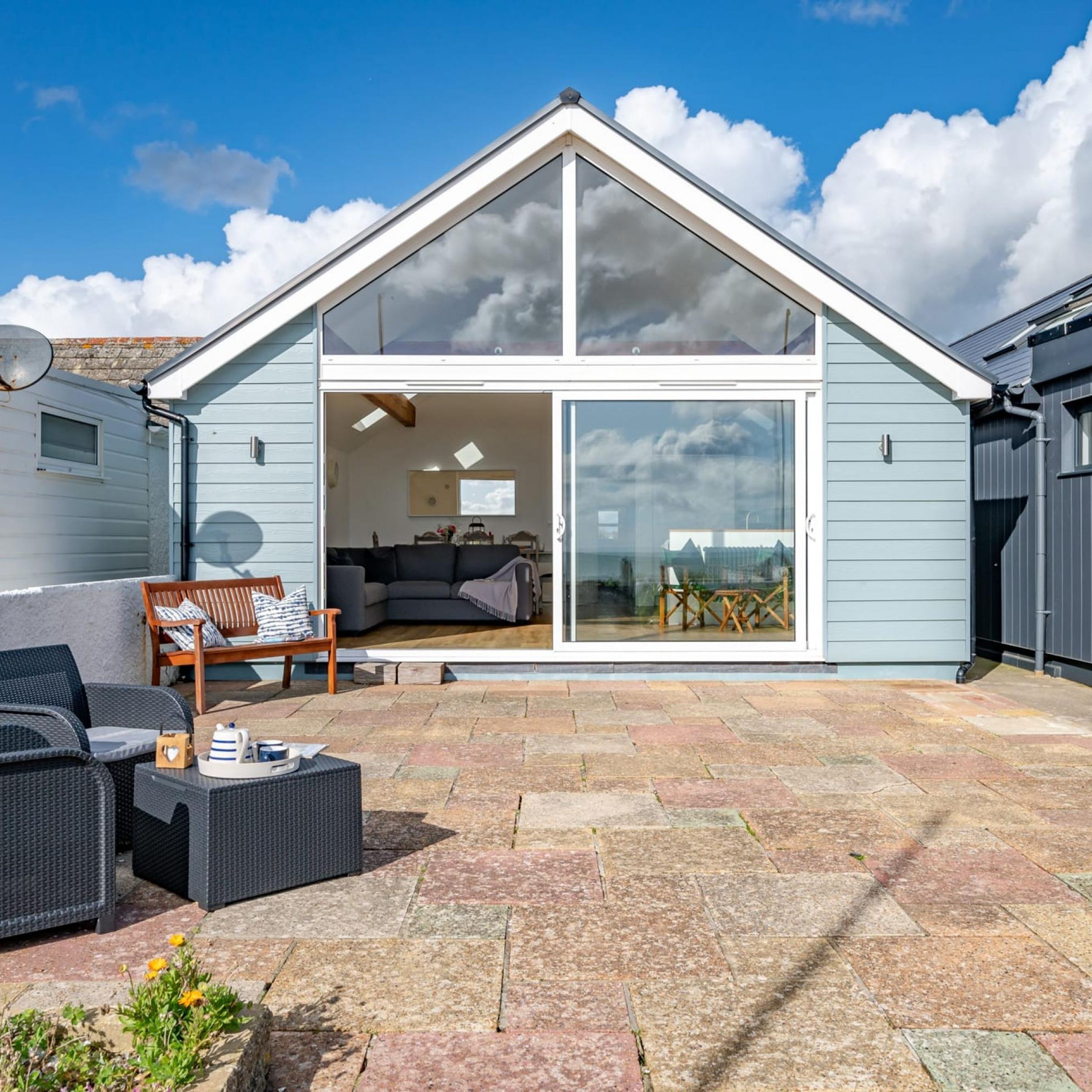 A modern house with a large glass sliding door leading to an interior with a sofa, a dining table, and a chair.