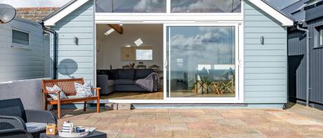 A modern house with a large glass sliding door leading to an interior with a sofa, a dining table, and a chair.