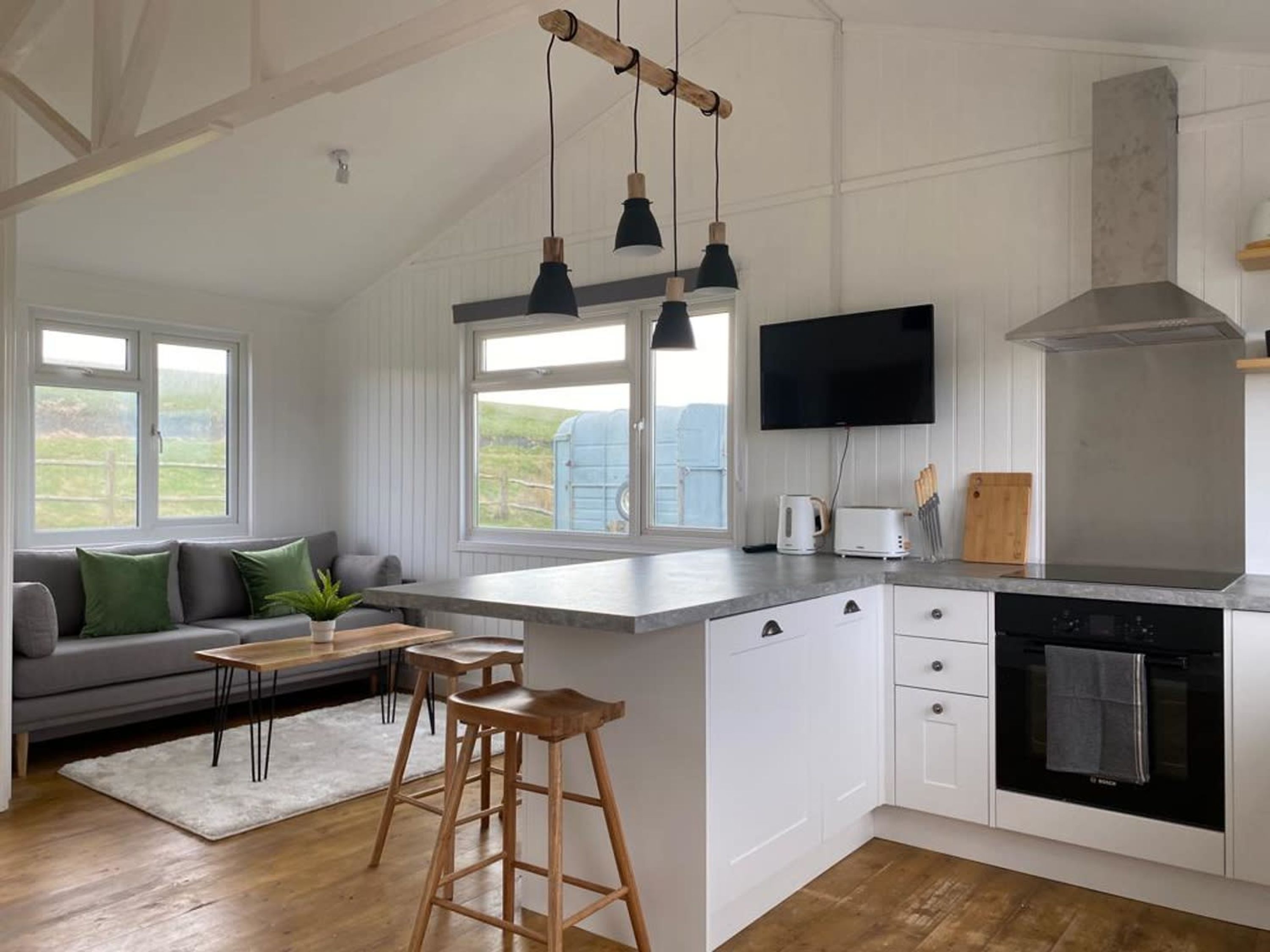 A modern kitchen with a large island, white cabinetry, a built-in oven, and a flat-screen TV.